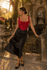 Corset rouge à bretelles porté avec jupe satin noire au Jardin du Luxembourg devant la fontaine Médicis à Paris à l’heure dorée