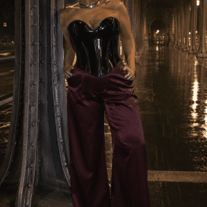 Bustier corset gothique moderne noir vernis porté avec un pantalon fluide satin bordeaux au Pont Bir-Hakeim à Paris lors d’une séance photo éditoriale de nuit sous une pluie fine.