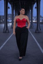 Femme élégante de 45 ans portant un bustier corset gothique rouge effet latex avec un pantalon tailleur noir large et des escarpins noirs au Pont Bir-Hakeim à Paris pendant la blue hour