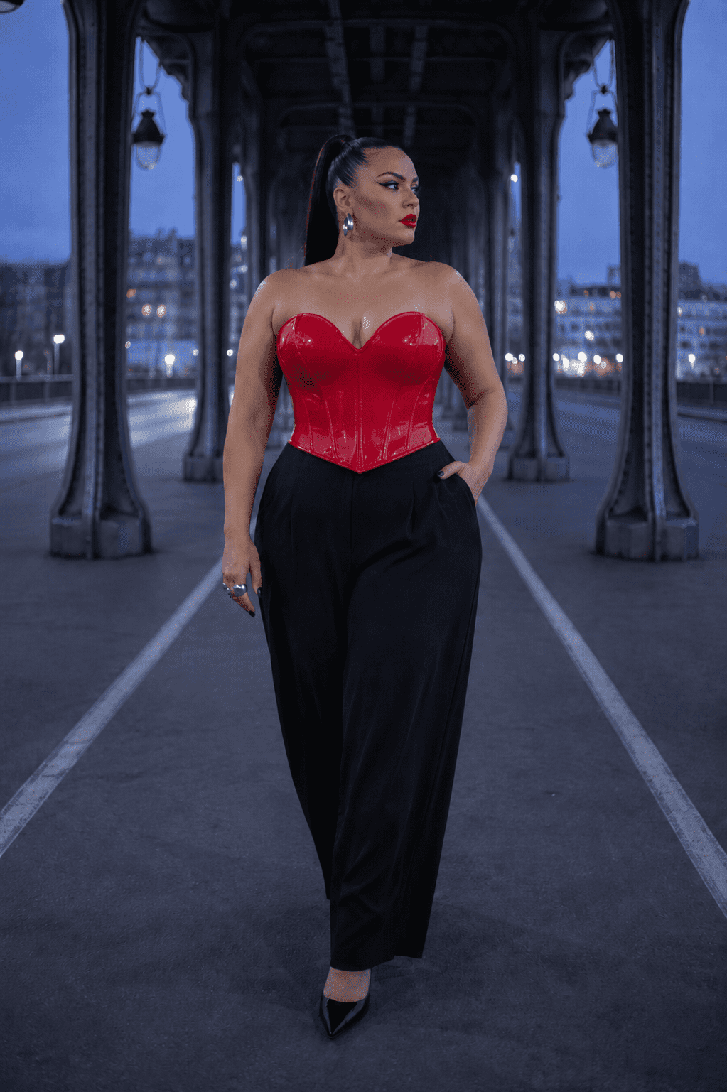 Femme élégante de 45 ans portant un bustier corset gothique rouge effet latex avec un pantalon tailleur noir large et des escarpins noirs au Pont Bir-Hakeim à Paris pendant la blue hour