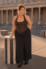 Femme grande taille 3XL portant un bustier corset marron steampunk avec pantalon noir large au Palais Royal près des Colonnes de Buren dans une ambiance éditoriale haute couture.