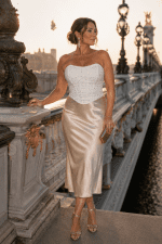 Femme élégante de 45 ans portant un corset bustier blanc à paillettes scintillantes avec jupe satin champagne au Pont Alexandre III à Paris pendant la golden hour