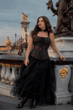 Femme de 40 ans portant un corset gothique noir et rouge à bretelles avec une longue jupe en tulle noire au Pont Alexandre III à Paris lors d’une séance photo éditoriale de mode