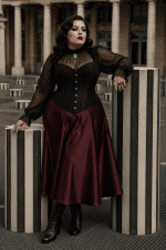Corset gothique noir grande taille porté avec une jupe midi satinée bordeaux au Palais Royal à Paris entre les colonnes de Buren dans un style éditorial élégant