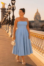 Femme élégante de 45 ans portant une robe midi bustier bleu ciel évasée photographiée au Pont Alexandre III à Paris pendant la golden hour dans une ambiance mode luxe éditoriale.