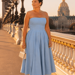 Femme élégante de 45 ans portant une robe midi bustier bleu ciel évasée photographiée au Pont Alexandre III à Paris pendant la golden hour dans une ambiance mode luxe éditoriale.