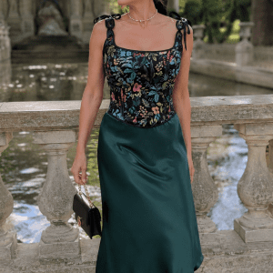 Femme de 45 ans portant un top style corset noir fleuri herbier avec une jupe midi satinée vert émeraude au Jardin du Luxembourg près de la fontaine Médicis dans une ambiance mode éditoriale élégante.