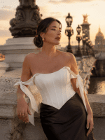 Femme de 40 ans portant un top corset satiné blanc style coquette avec jupe midi satinée noire au Pont Alexandre III à Paris au golden hour dans un style éditorial haute couture.