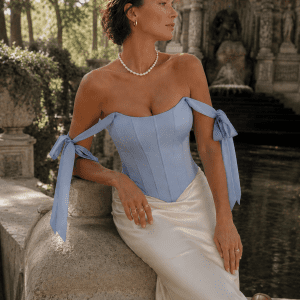 Femme de 40 ans portant un top corset satiné bleu pastel avec jupe midi satinée écrue au Jardin du Luxembourg devant la fontaine Médicis à Paris.