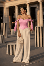 Femme de 40 ans portant un top corset satiné rose pastel avec pantalon large crème au Palais Royal à Paris dans un style éditorial mode élégant.