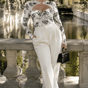 Femme de 45 ans portant un bustier corset blanc à imprimé floral noir avec manches longues, associé à un pantalon de tailleur ivoire large devant la Fontaine de Médicis au Jardin du Luxembourg.