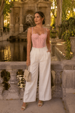 Femme portant un bustier corset rose pastel en dentelle avec pantalon large écru à la Fontaine de Médicis à Paris au coucher du soleil