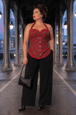 Photo de mode éditoriale réalisée au Pont Bir-Hakeim à Paris à la blue hour mettant en scène un corset bustier écossais rouge et gris à motif tartan. Le corset est associé à un pantalon de tailleur noir fluide, des bottines pointues en cuir noir, des créoles métalliques et un sac baguette noir, dans une ambiance élégante inspirée de la haute couture parisienne.