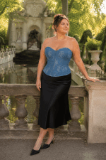 Femme de 45 ans portant un corset bustier en jean bleu à motif de roses avec une jupe midi satinée noire devant la fontaine de Médicis au Jardin du Luxembourg à Paris