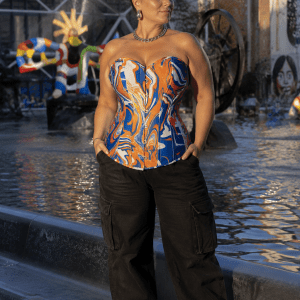 Femme de 45 ans portant un corset bustier psychédélique bleu roi, orange et blanc avec un pantalon cargo noir sur la place Igor-Stravinsky à Paris, devant la fontaine Stravinsky au coucher du soleil.