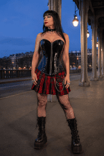 Corset bustier noir en latex brillant avec fermeture éclair argentée sur le devant, porté avec une minijupe écossaise rouge et noire au pont Bir-Hakeim à Paris à la blue hour
