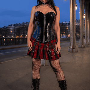 Corset bustier noir en latex brillant avec fermeture éclair argentée sur le devant, porté avec une minijupe écossaise rouge et noire au pont Bir-Hakeim à Paris à la blue hour