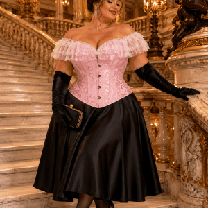 Femme de 40 ans en corset bustier victorien rose grande taille avec dentelle blanche, jupe midi noire satinée et gants d’opéra noirs sur le grand escalier du Palais Garnier à Paris.