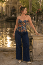Femme de 40 ans portant un corset bustier bleu style jean à imprimé floral vintage avec un jean large taille haute indigo foncé à la Fontaine de Médicis au Jardin du Luxembourg à Paris, lumière golden hour du matin.