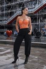 Corset bustier transparent orange porté avec un pantalon cargo noir fluide lors d'une séance photo mode contemporaine à la place Igor Stravinsky à Paris.