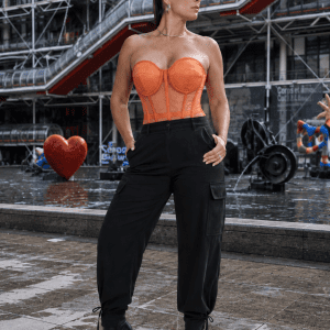 Corset bustier transparent orange porté avec un pantalon cargo noir fluide lors d'une séance photo mode contemporaine à la place Igor Stravinsky à Paris.