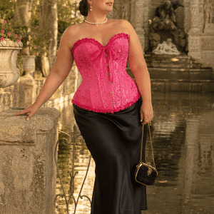 Femme de 40 ans portant un corset bustier victorien rose grande taille avec motif jacquard ton sur ton, jupe midi noire en satin et bottines victoriennes à la Fontaine de Médicis à Paris.