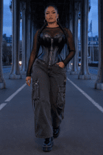 corset gothique noir en similicuir avec zip frontal argenté, coupe bustier cœur, baleinage apparent et attaches pour porte-jarretelles, porté avec un pantalon cargo large gris anthracite sur le pont Bir-Hakeim à Paris