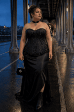 Femme élégante de 40 ans taille 3XL portant un corset noir brocart floral grande taille avec une jupe maxi en satin noir au pont Bir-Hakeim à Paris pendant la blue hour.