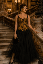 Femme élégante de 40 ans portant un corset noir et jaune ocre médiéval gothique avec jupe longue en tulle noir dans le grand escalier du Palais Garnier à Paris sous une lumière dorée.