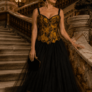 Femme élégante de 40 ans portant un corset noir et jaune ocre médiéval gothique avec jupe longue en tulle noir dans le grand escalier du Palais Garnier à Paris sous une lumière dorée.