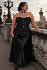 Corset noir fleuri grande taille en jacquard ton sur ton, avec fermeture à busc métallique sur le devant et coupe cintrée mettant en valeur la silhouette. Présenté dans un look élégant avec une jupe longue en satin noir lors d'une séance photo éditoriale au Pont Alexandre III à Paris.