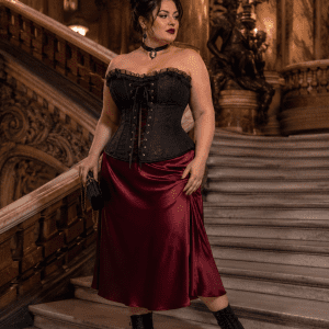 Femme de 40 ans taille 3XL portant un corset noir néo-victorien grande taille avec jupe midi satin bordeaux dans le grand escalier du Palais Garnier à Paris.
