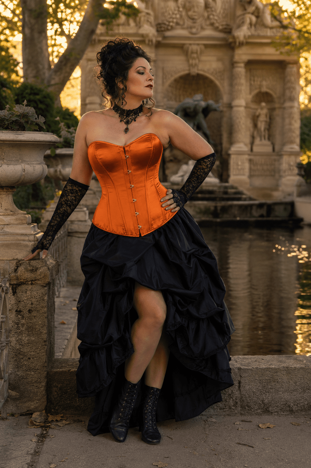 Femme de 45 ans portant un corset orange écarlate satiné néo-victorien avec jupe asymétrique noire en taffetas à la Fontaine de Médicis à Paris durant la golden hour du matin.