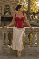 Femme portant un corset soutien-gorge rouge bordeaux en dentelle avec une jupe midi satin champagne à la fontaine de Médicis à Paris