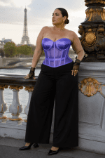 Femme de 40 ans taille 3XL portant un corset transparent violet grande taille à effet satin et tulle, associé à un pantalon palazzo noir taille haute sur le pont Alexandre III à Paris, avec la tour Eiffel floutée en arrière-plan.