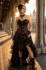 Photo de mode éditoriale au Pont Bir-Hakeim à Paris mettant en scène un corset steampunk victorien noir et rouge à panneaux contrastés et laçages décoratifs, porté avec une jupe asymétrique en tulle noir, des bottines victoriennes et des accessoires gothiques raffinés dans une lumière dorée de fin d’après-midi.