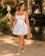 Robe bustier corset blanche fleurie style coquette avec imprimé bleu pastel, fines bretelles, détail noué à la poitrine et jupe évasée bordée de dentelle.