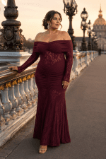 Femme de 45 ans portant une robe longue de soirée sirène bordeaux avec épaules dénudées, manches longues en dentelle florale et coupe élégante au Pont Alexandre III à Paris.