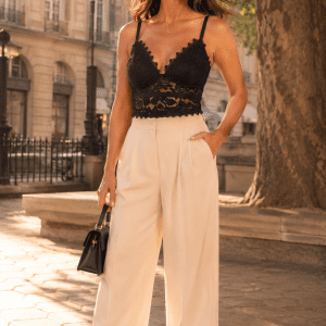 Femme de 40 ans portant un soutien-gorge corset noir en dentelle florale avec pantalon fluide crème taille haute à la place Dauphine à Paris sous la lumière dorée de fin d'après-midi.
