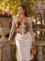 Femme de 45 ans portant un top corset blanc cassé fleuri à manches longues en dentelle avec une jupe midi satin crème devant la fontaine de Médicis au Jardin du Luxembourg.