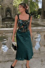 Femme de 45 ans portant un top style corset noir fleuri herbier avec une jupe midi satinée vert émeraude au Jardin du Luxembourg près de la fontaine Médicis dans une ambiance mode éditoriale élégante.