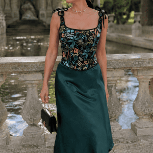 Femme de 45 ans portant un top style corset noir fleuri herbier avec une jupe midi satinée vert émeraude au Jardin du Luxembourg près de la fontaine Médicis dans une ambiance mode éditoriale élégante.