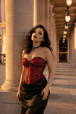 Bustier corset gothique rouge à broderies dorées porté avec une jupe longue noire satinée sous les arcades de la galerie Valois au Palais-Royal, à Paris, dans une lumière dorée de fin de journée.