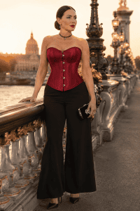 Femme portant un corset rouge satiné avec un pantalon noir, une pochette élégante et des accessoires discrets sur le Pont Alexandre III à Paris.