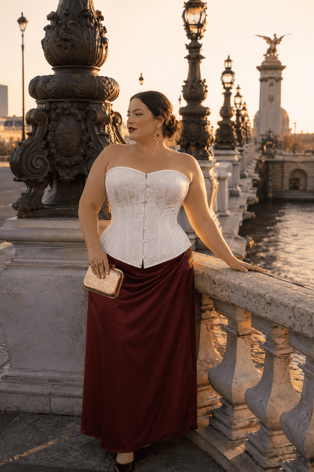Femme élégante de 40 ans portant un corset blanc vénitien grande taille en jacquard floral avec jupe satinée bordeaux au Pont Alexandre III à Paris pendant la golden hour