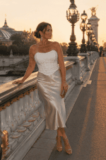 Femme élégante de 45 ans portant un corset bustier blanc à paillettes scintillantes avec jupe satin champagne au Pont Alexandre III à Paris pendant la golden hour