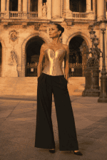 Corset bustier steampunk doré métallique porté avec un pantalon palazzo noir sur le parvis du palais garnier à Paris au coucher du soleil.