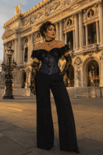 Corset gothique bleu nuit en satin et dentelle noire porté avec un pantalon palazzo noir devant le palais garnier à Paris durant la golden hour du soir