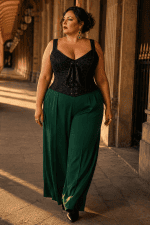Corset gothique noir à lacets grande taille avec bretelles larges réglables, porté avec un pantalon fluide vert émeraude taille haute dans la Galerie de Montpensier au Palais-Royal à Paris, lumière dorée de fin de journée.