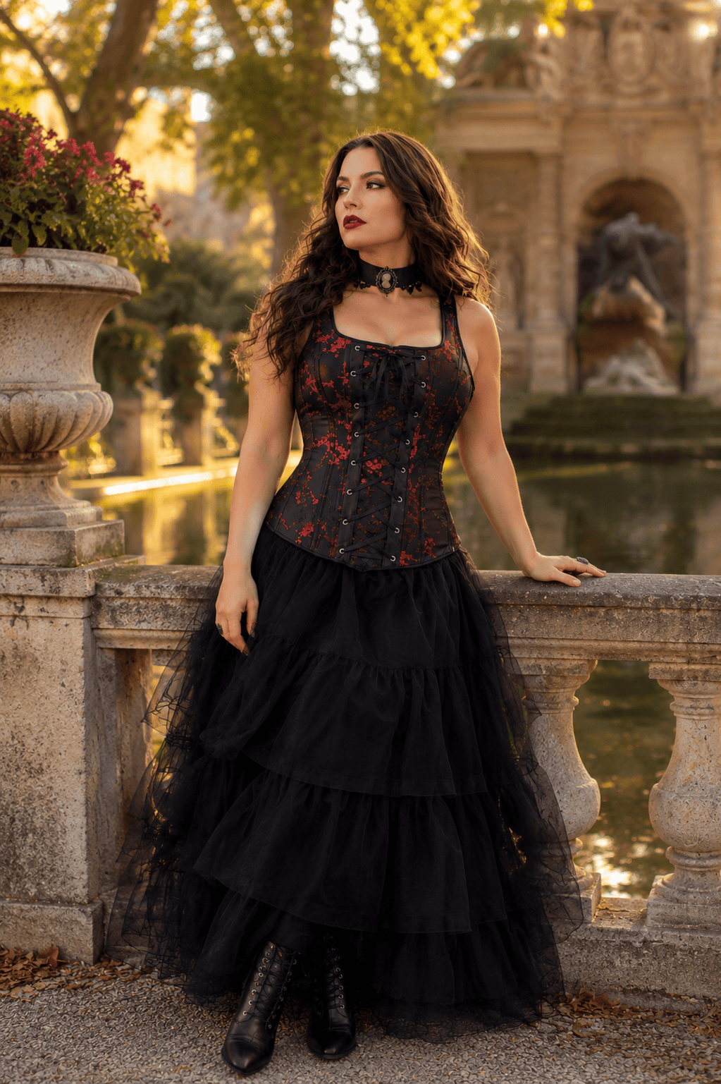 Femme de 40 ans portant un corset gothique noir et rouge à bretelles avec une longue jupe en tulle noire a la fontaine de medicis a Paris lors d’une séance photo éditoriale de mode